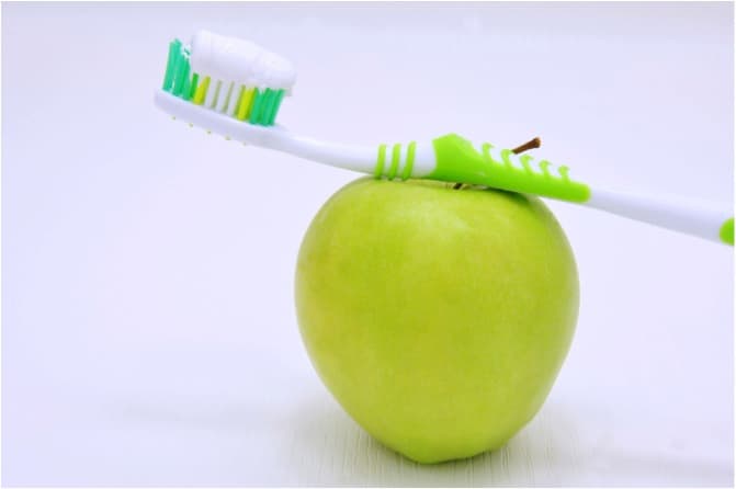 A toothbrush with toothpaste leaning on a small green apple.