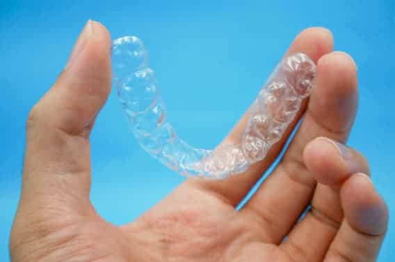 A hand holding a pair of Invisalign clear aligners in front of a blue background