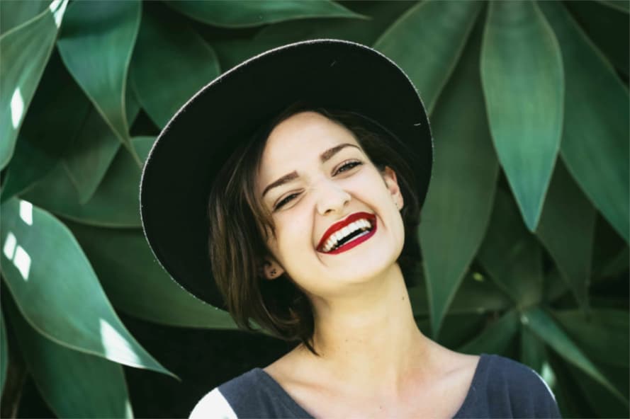 A woman standing in front of a green plant and smiling.