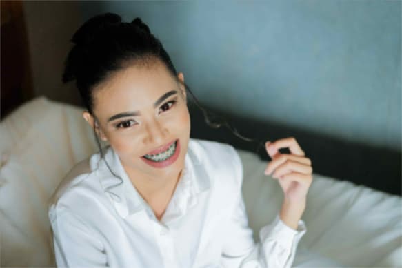 A woman sitting on a bed and smiling with metal braces on her teeth
